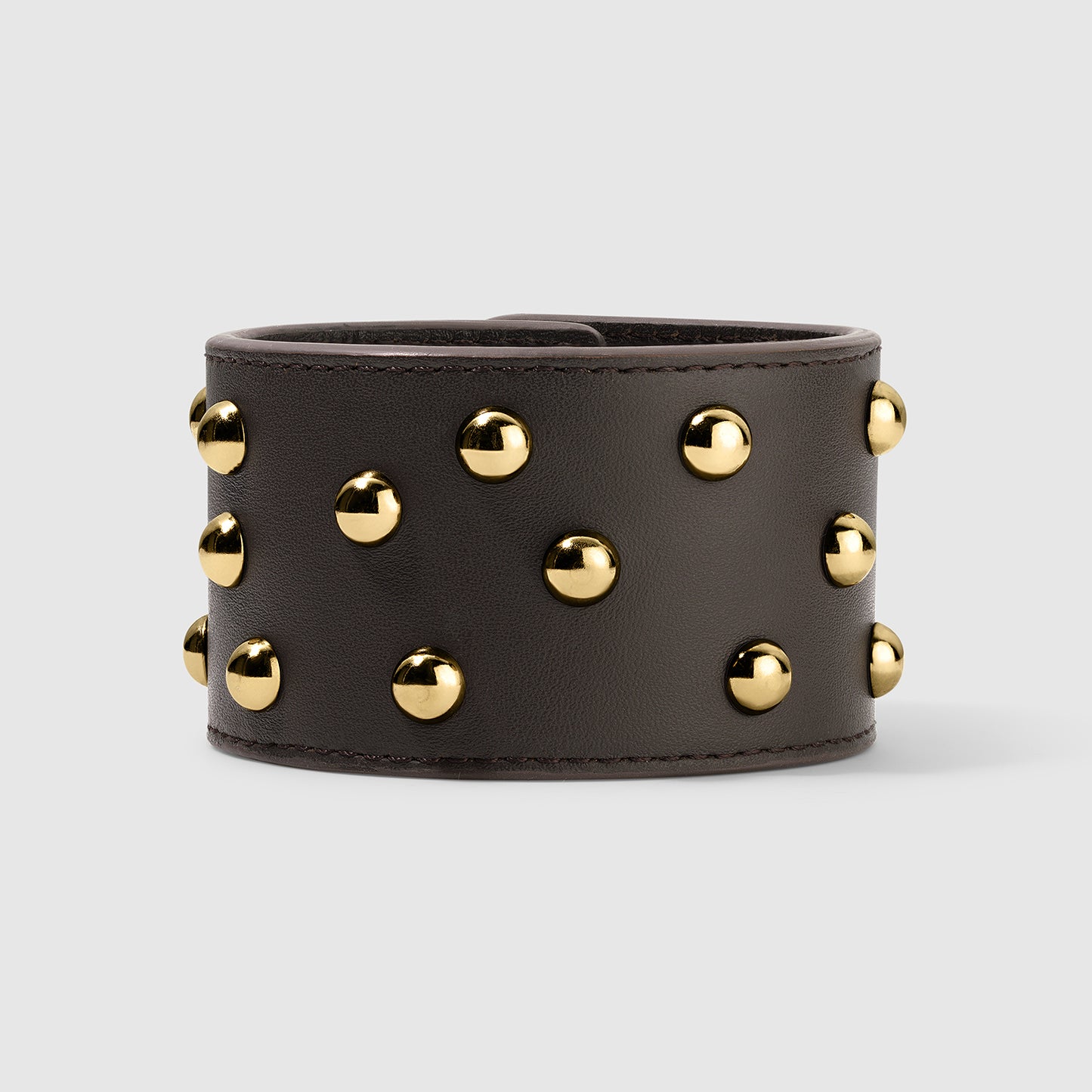 Wide brown leather cuff bracelet adorned with evenly spaced gold dome studs, showcasing a bold and edgy design. The bracelet has a smooth finish and structured edges, displayed on a light gray background.
