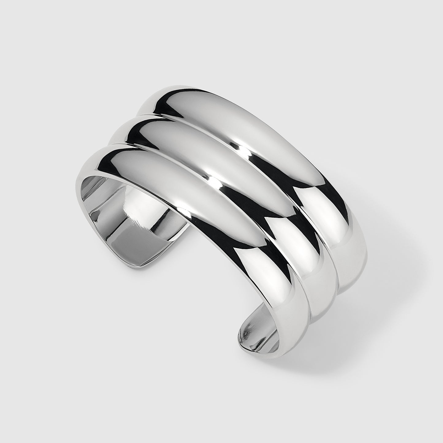 Side view of a silver cuff bracelet with a polished finish and three stacked horizontal bands, showcasing its modern and reflective design on a light gray background.